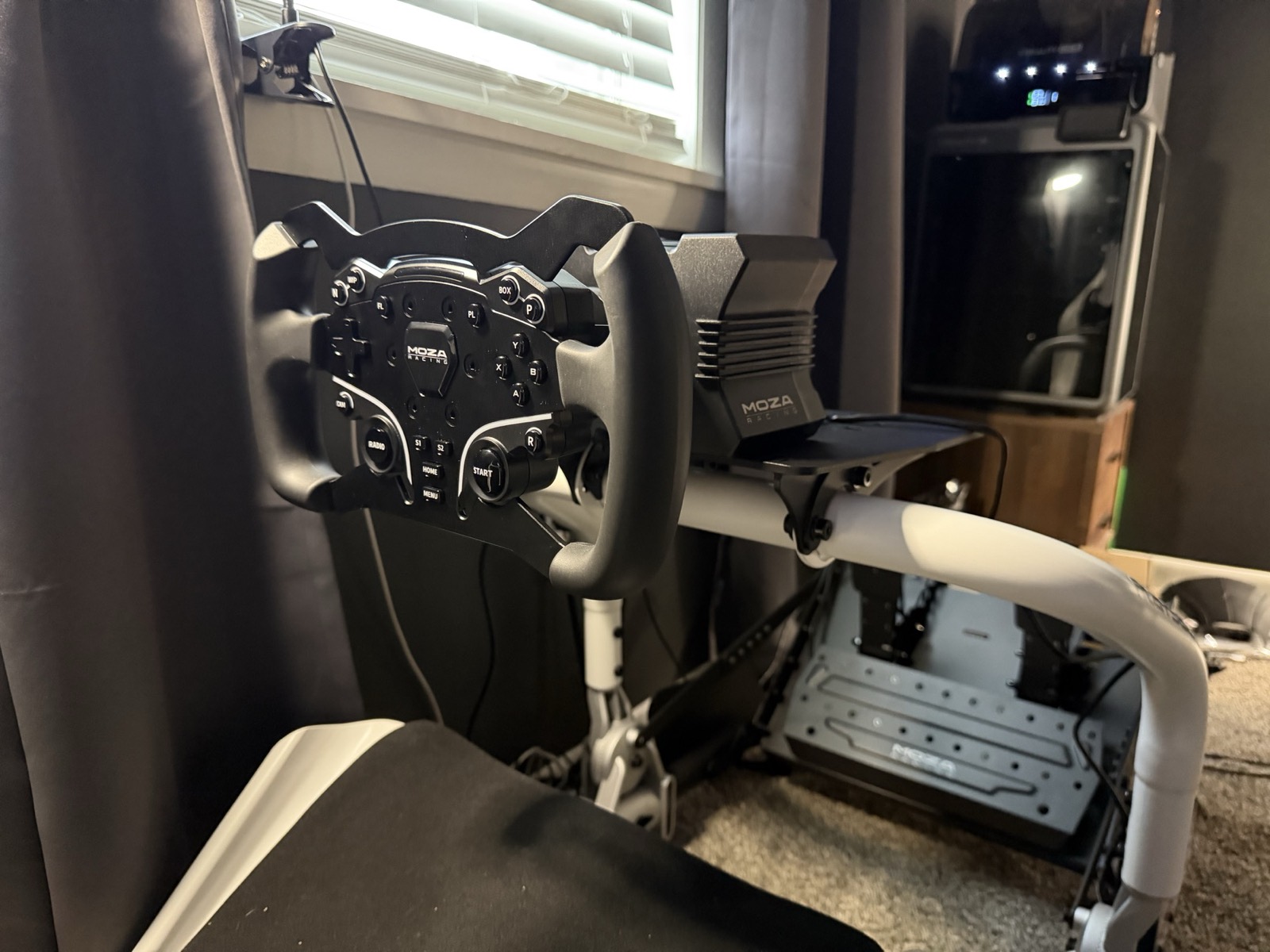 The first set: a Moza R5 base with the CS wheel on the Playseat wheel deck, window light behind.